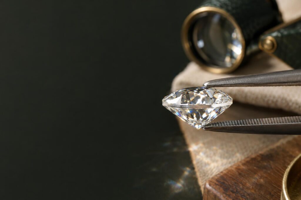 Macro of a diamond's girdle edge with a faint laser inscription held in tweezers beside a loupe