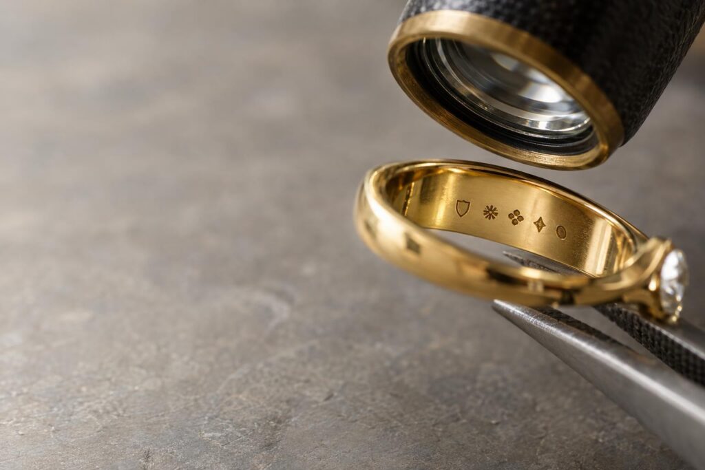 Gold ring interior with tiny punched marks seen through a jeweller's loupe held in tweezers