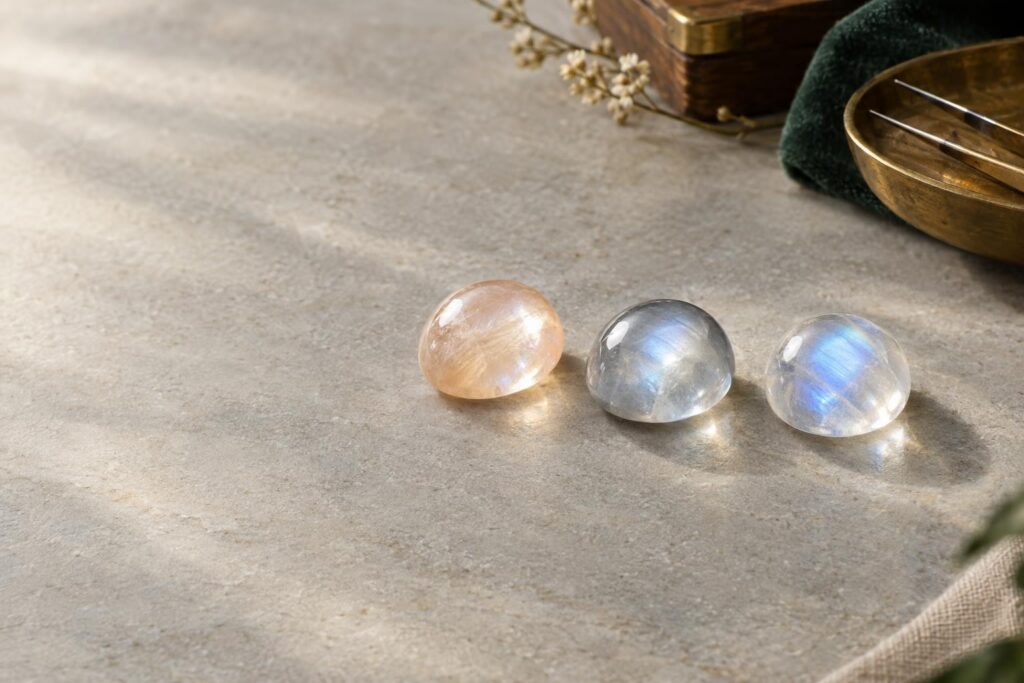 Three moonstone cabochons in peach, grey and colourless bodycolours showing different sheen