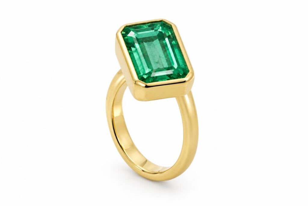 Step-cut emerald ring with a smooth metal bezel rim wrapping the whole edge of the stone